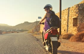 Een toerist die wegrijdt op een scooter en achterom kijkt