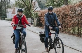 Een man en vrouw met fietshelm op fietsen op elektrische fietsen.