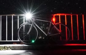 Een fiets met brandend voorlicht en achterlicht die tegen een hek aanstaat