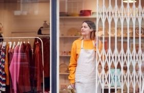 Een winkelmedewerker staat voor de winkel, met het anti-inbraak-hekwerk van de winkel halfgeopend.