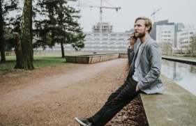 Een man zit te bellen op de rand van een verhoogde vijver in een stadspark.