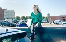 Marjolein Groen, directeur Sustainability en CSR bij mobiliteitsprovider Athlon Nederland, draagt een groene bloes en zit lachend op een parkeerplaats