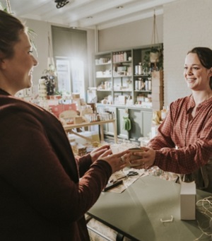 Een winkelier geeft een ingepakt doosje aan een klant, terwijl ze allebei vrolijk kijken.