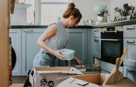 Een vrouw zit op haar knieën in de keuken bij verhuisdozen